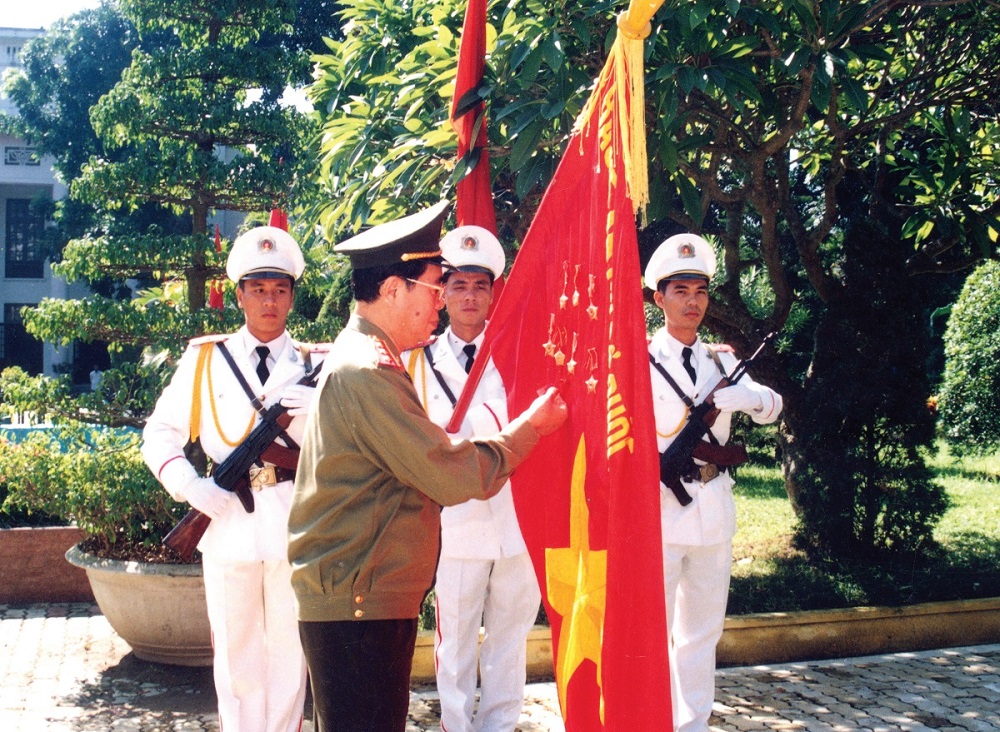 Đồng chí Thượng tướng Lê Minh Hương - Ủy viên Bộ Chính trị, Bộ trưởng Bộ Công an gắn Huân chương Lao động hạng Ba lên lá cờ truyền thống của Trường Đại học An ninh nhân dân, năm 2001